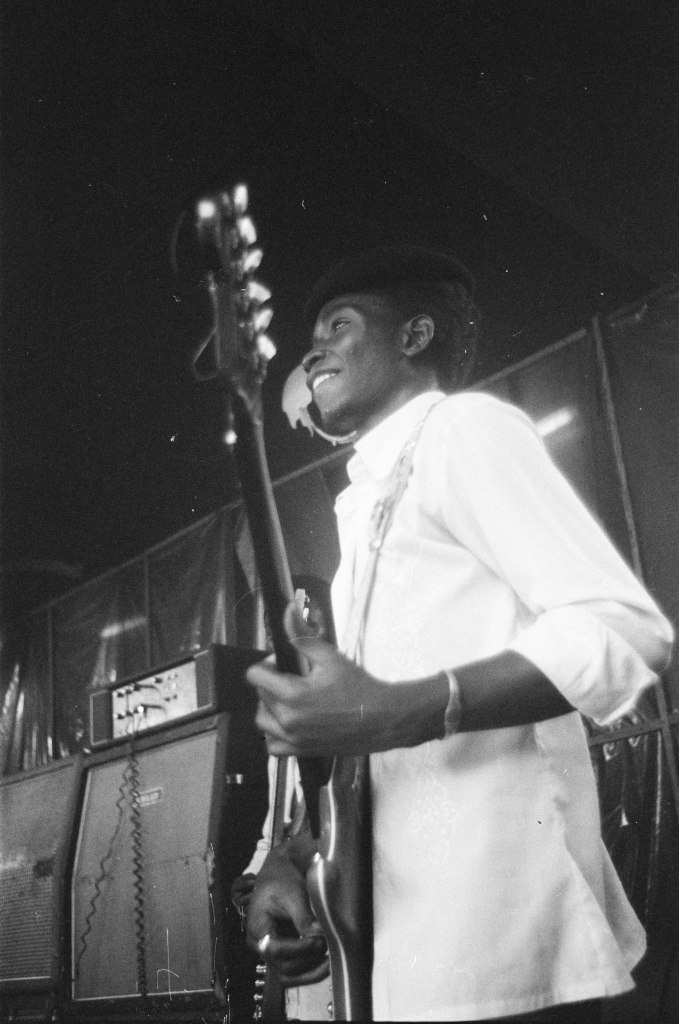 nigerian bass player smiling wearing beret with amplifiers behind