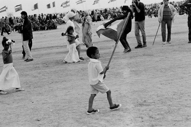 boy carries flag at polisario ten year celebration western sahara 1986 with crowd in background