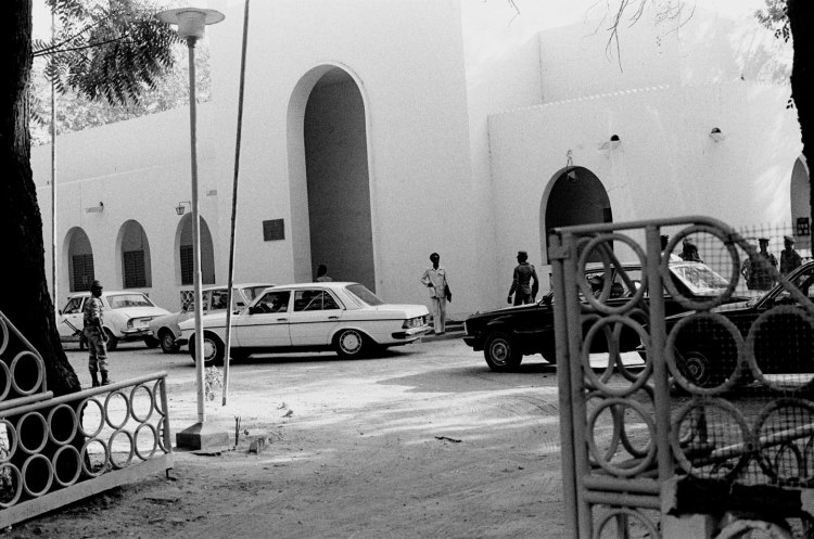 view through gates to cars and soldiers outside modern building with arched openings ndjamena 1982