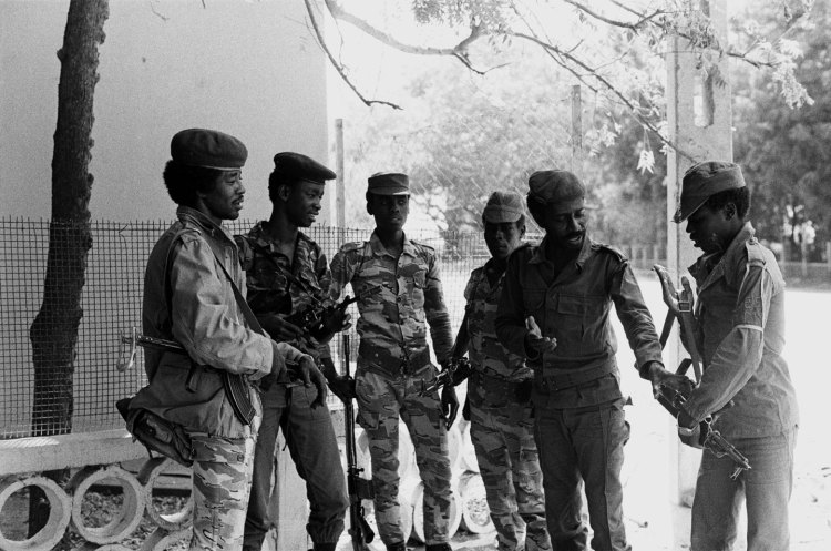 four chadian soldiers watch as two others pass a gun