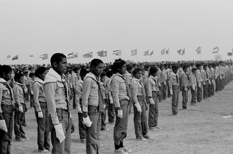 teenagers in uniform stand in lines at polisario ten year celebration western sahara 1986 with flags behind
