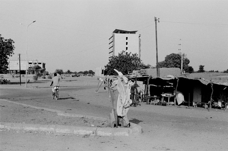 cyclist in street with shanty town and apartment building in background ndjamena 1982