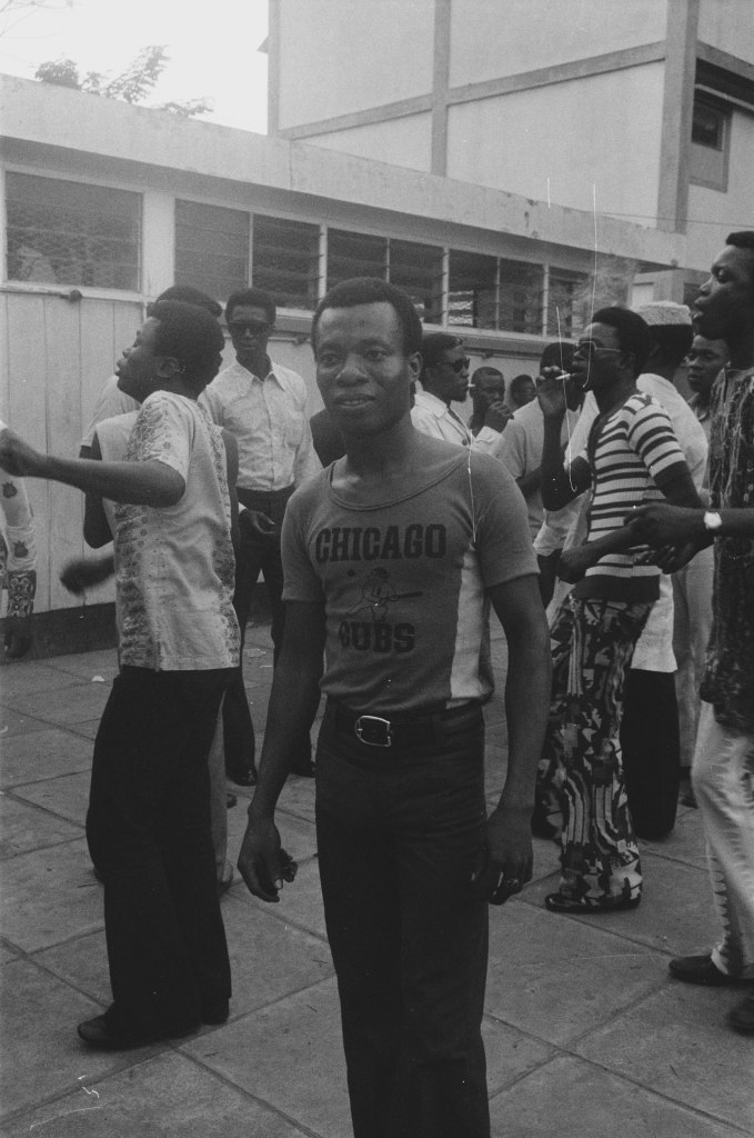 portrait of a young man wearing a chicago t shirt with boys in the yard behind in lagos 1978