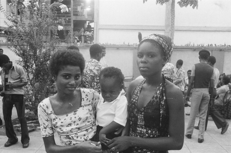 two nigerian girls with baby surrounded by boys and men in the yard at the shrine nightclub in lagos shrub in background 1978