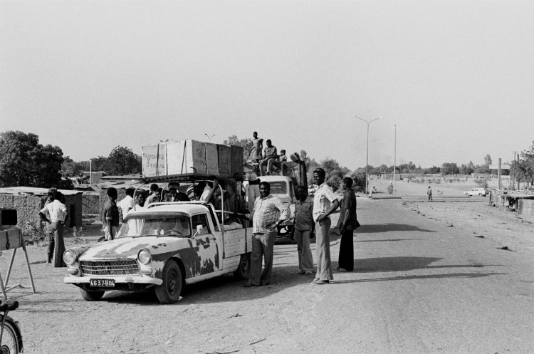 truck piled high with boxes and men standing around road in chad 1982