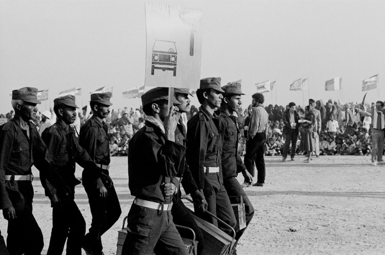men marching in military uniforms with car banner polisario ten year celebration western sahara 1986